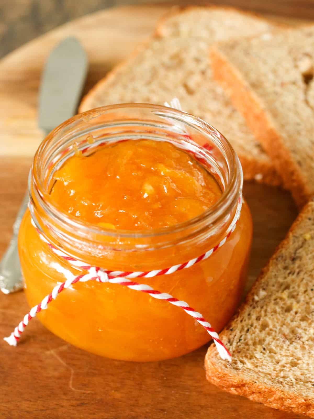 Mango Jam in a mason jar with wheat bread slices in the background.