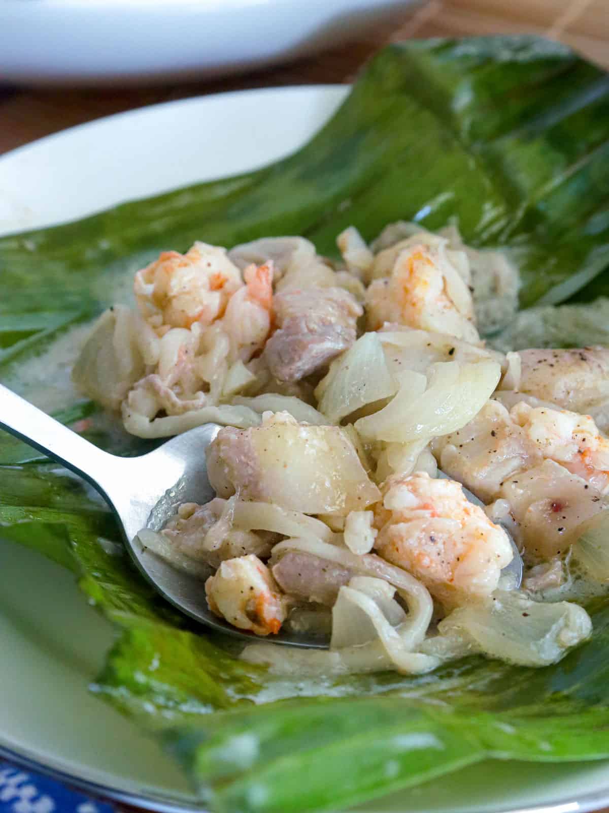 eating pinais na hipon with a spoon on a banana leaf-lined white plate.